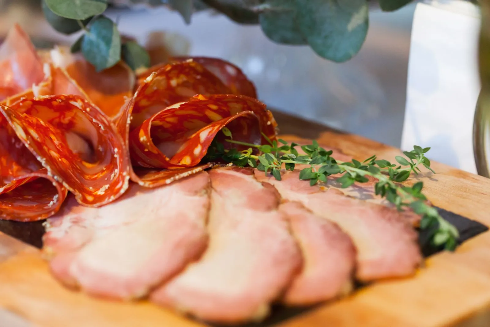 Delicious assortment of cured meats and fresh herbs on a wooden board, perfect for appetizers.